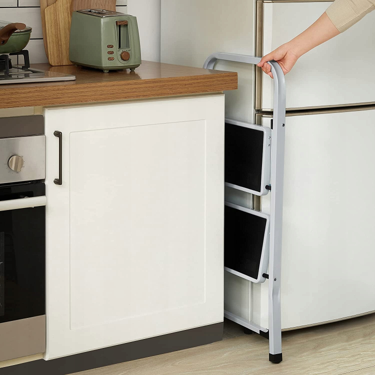 Osoba trzyma składana drabina dwustopniowa z białą ramą i czarnymi stopniami.